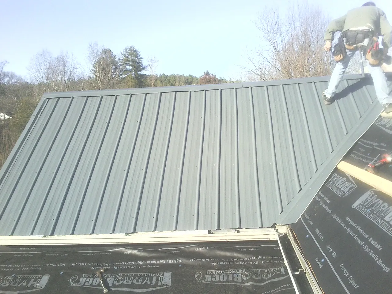 Crew installing dark green standing seam panels over synthetic underlayment in Buffalo